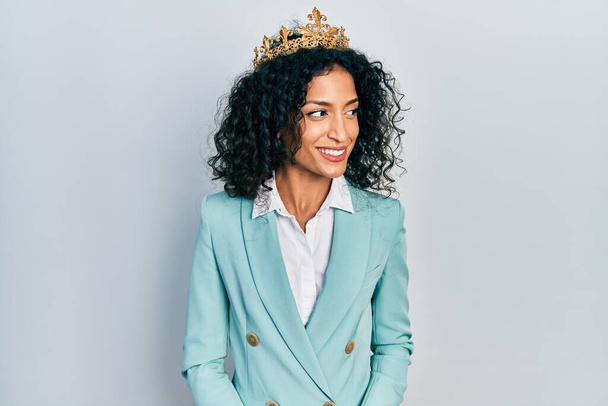 Young latin girl wearing business clothes and queen crown looking away to side with smile on face, natural expression. laughing confident.  - Фото, зображення