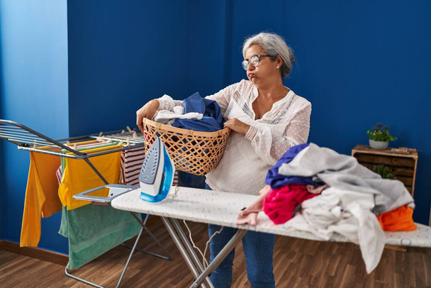 Kobieta w średnim wieku zestresowana wykonywaniem prac domowych w pralni - Zdjęcie, obraz