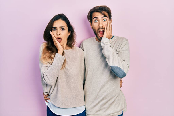 Jovem casal hispânico vestindo roupas casuais com medo e chocado, surpresa e expressão espantada com as mãos no rosto  - Foto, Imagem