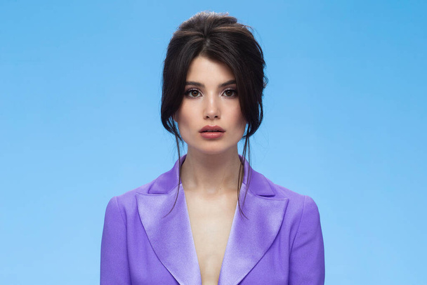 Side view of a sexy brunette in a stylish purple suit in attractive, looking at camera, isolated blue background. - Φωτογραφία, εικόνα