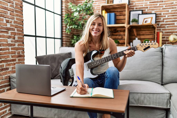 Mladá blondýnka žena usměvavá sebevědomě hraje elektrickou kytaru doma - Fotografie, Obrázek