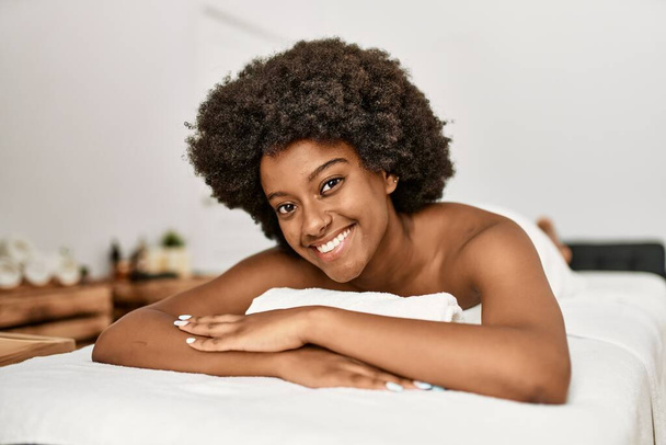 Giovane donna afroamericana sorridente fiducioso sdraiato sul lettino da massaggio al centro di bellezza - Foto, immagini