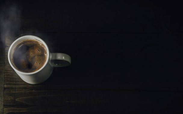 Белая кружка с горячим напитком. Чашка кофе на тёмном деревянном столе. Вид сверху, пространство для копирования текста. - Фото, изображение