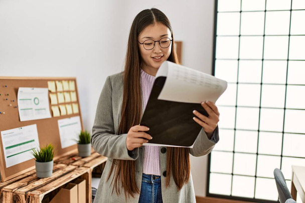 Young chinese businesswoman reading document on clipboard at the office. - Φωτογραφία, εικόνα