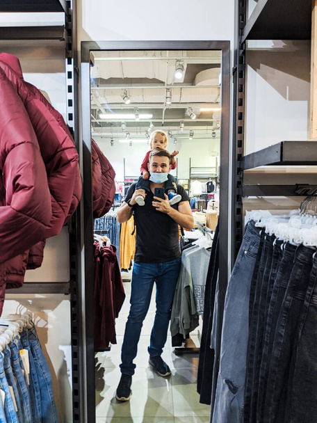 Dad with a little girl on his shoulders is photographed in a mirror in a clothing store. High quality photo - Foto, imagen