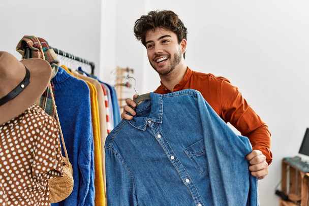 Genç İspanyol müşteri gülümsüyor. Giysi mağazasında tişörtlü bir askı tutuyor.. - Fotoğraf, Görsel