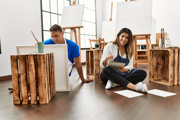 Δύο μαθητές χαμογελώντας χαρούμενη ζωγραφική κάθεται στο πάτωμα στη σχολή καλών τεχνών. - Φωτογραφία, εικόνα
