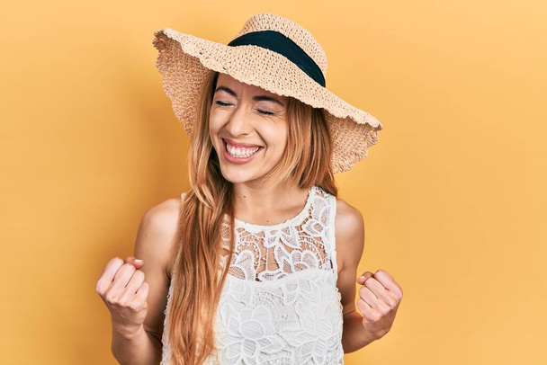 Młoda biała kobieta w letniej czapce podekscytowana sukcesem z podniesionymi ramionami i zamkniętymi oczami świętującymi zwycięstwo uśmiechnięta. koncepcja zwycięzcy.  - Zdjęcie, obraz