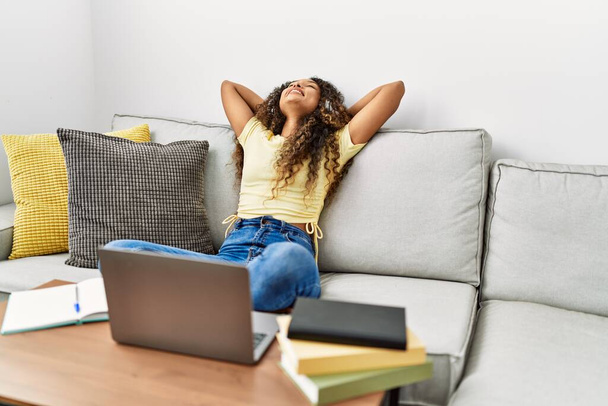Giovane donna latina rilassata con le mani sulla testa utilizzando il computer portatile a casa - Foto, immagini