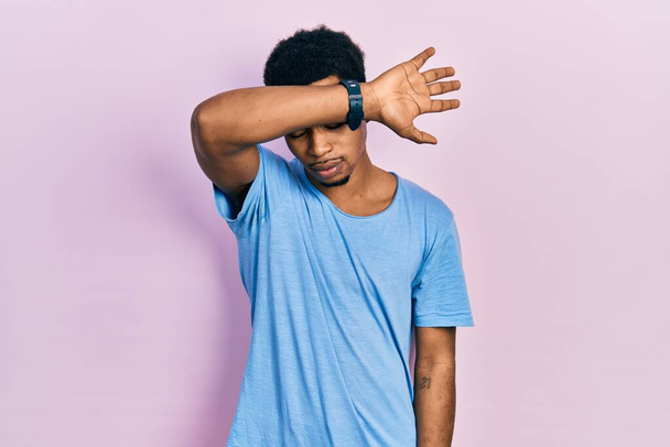 Νεαρός Αφροαμερικάνος που φοράει μπλε μπλουζάκι που καλύπτει τα μάτια με το χέρι, δείχνει σοβαρός και λυπημένος. έννοια της μη παρατήρησης, της απόκρυψης και της απόρριψης  - Φωτογραφία, εικόνα