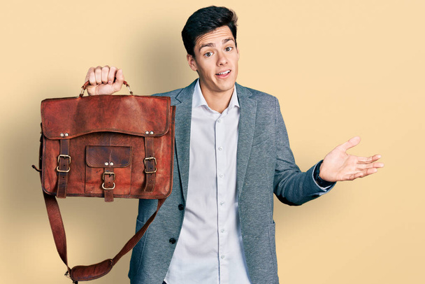 Young hispanic man holding business bag celebrating achievement with happy smile and winner expression with raised hand  - Фото, зображення