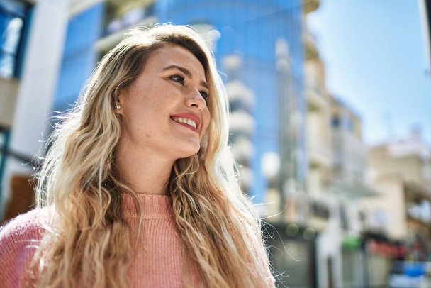 Young blonde woman smiling at the city - 写真・画像