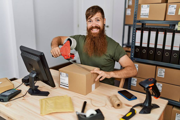 Genç kızıl saçlı iş adamı ofiste karton kutu paketliyor. - Fotoğraf, Görsel