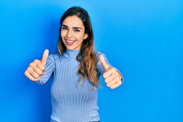 Young hispanic girl wearing casual clothes approving doing positive gesture with hand, thumbs up smiling and happy for success. winner gesture.  - Photo, Image