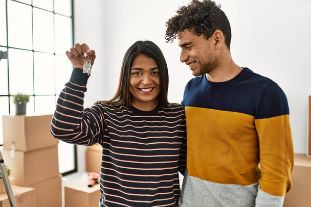 Молодая латинская пара улыбается счастливой и обнимается, держа ключ от нового дома. - Фото, изображение