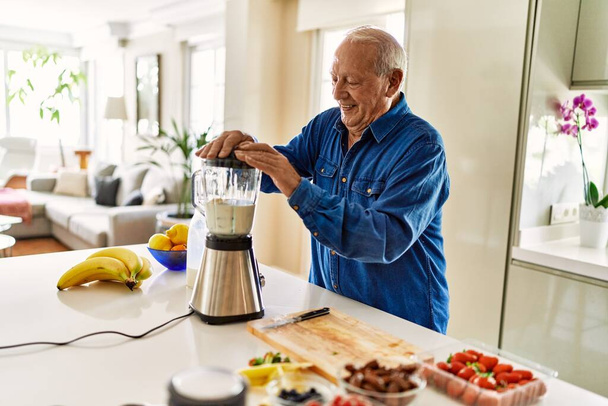 Senior man smiling confident shaking blender at kitchen - Фото, изображение