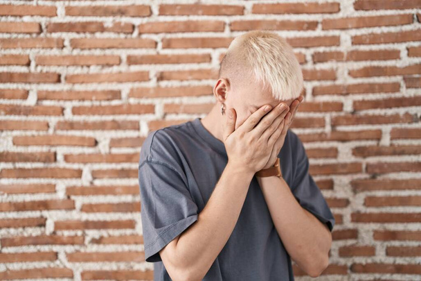 Young caucasian man standing over bricks wall with sad expression covering face with hands while crying. depression concept.  - Fotografie, Obrázek