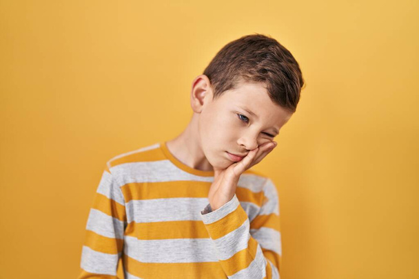 Jeune enfant caucasien debout sur fond jaune pensant fatigué et ennuyé avec des problèmes de dépression avec les bras croisés.  - Photo, image