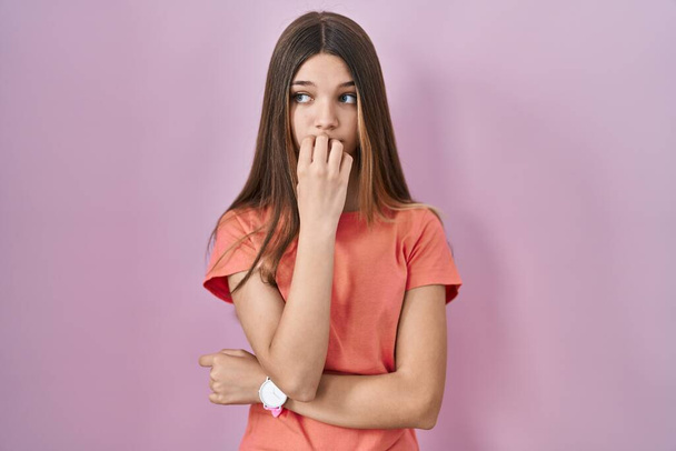 Teenager girl standing over pink background looking stressed and nervous with hands on mouth biting nails. anxiety problem.  - Fotografie, Obrázek
