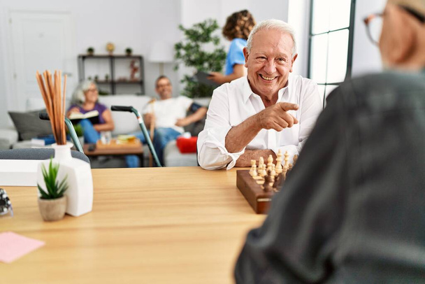 Kaksi eläkeläistä hymyilee onnellisena pelatessaan shakkia hoitokodissa.. - Valokuva, kuva