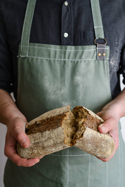 Crispy fresh bread in the hands of a man. Rustic organic wheat bread. Gluten free. Home baking bread closeup. Delicious natural foods, healthy food baking. Small business and slow food concept - Fotó, kép