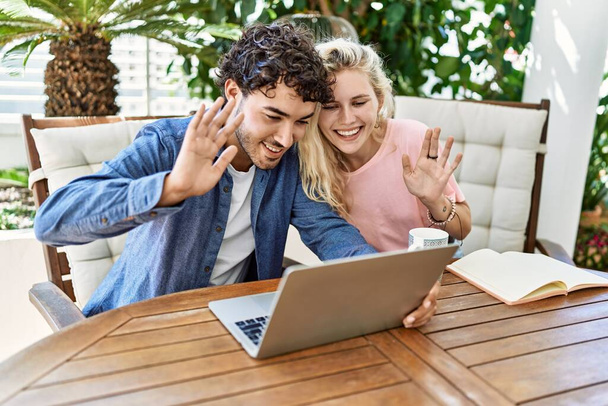 Молода пара посміхається щасливий відеодзвінок за допомогою ноутбука, що сидить на столі на терасі
. - Фото, зображення