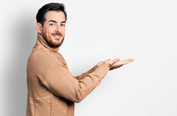 Fiatal spanyol férfi alkalmi ruhát visel, félrenézve nyitott tenyérrel, fénymásoló hellyel, vidáman mosolygó hirdetéssel.  - Fotó, kép