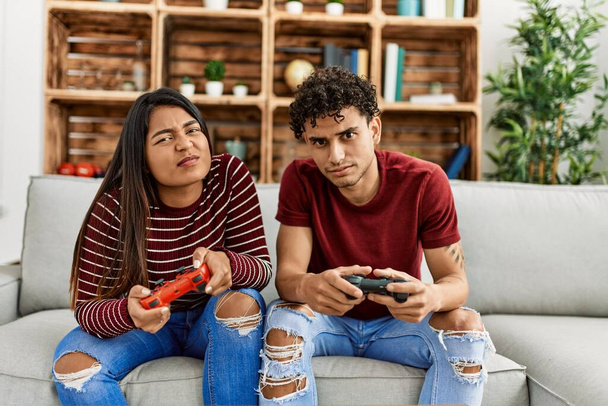 Young latin couple unhappy playing video game sitting on the sofa at home. - Φωτογραφία, εικόνα