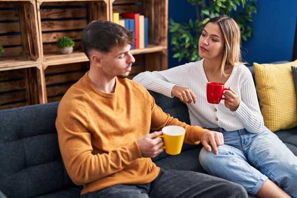 Young man and woman couple drinking coffee sitting on sofa at home - Fotografie, Obrázek