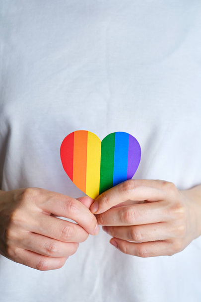 Rainbow heart from paper in woman hands in white t-shirt. LGBT flag. LGBTQIA Pride Month in June. Lesbian Gay Bisexual Transgender. Gender equality. Human rights and tolerance. Rainbow flag - Photo, image