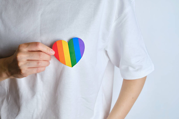 Rainbow heart from paper in woman hands in white t-shirt. LGBT flag. LGBTQIA Pride Month in June. Lesbian Gay Bisexual Transgender. Gender equality. Human rights and tolerance. Rainbow flag - Photo, image