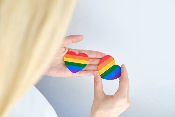 Rainbow heart from paper in woman hands in white t-shirt. LGBT flag. LGBTQIA Pride Month in June. Lesbian Gay Bisexual Transgender. Gender equality. Human rights and tolerance. Rainbow flag - Foto, Bild