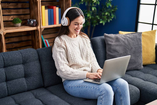 Young woman using laptop and headphones sitting on sofa at home - Photo, image