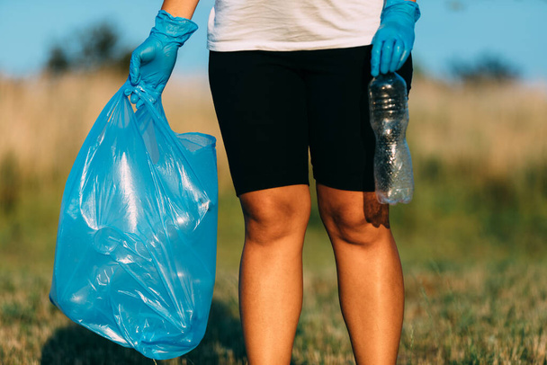 Plastic pollution in the environmental problem of the world. A hand in a blue glove puts garbage in a plastic bag. Removal and cleaning of garbage from contaminated territories - 写真・画像