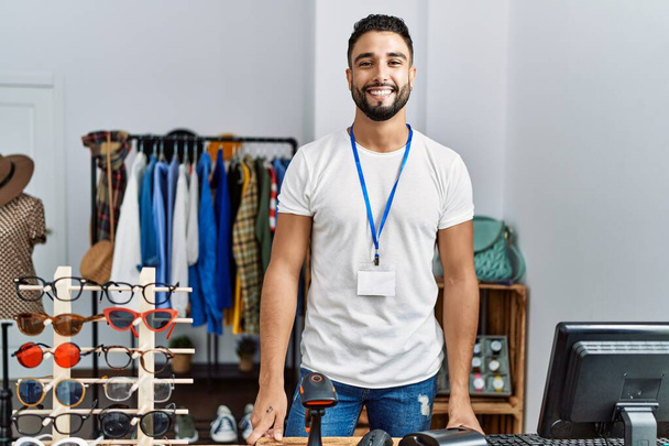 Joven árabe hombre tendero sonriendo confiado trabajando en tienda de ropa - Foto, imagen