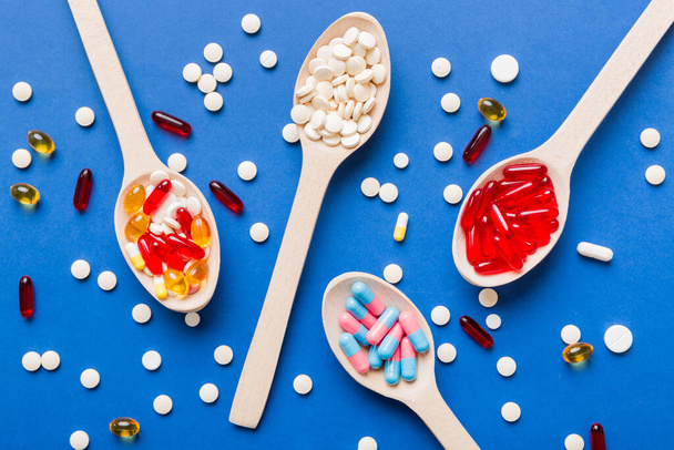 Vitamin capsules in a spoon on a colored background. Pills served as a healthy meal. Red soft gel vitamin supplement capsules on spoon. - Foto, Imagen