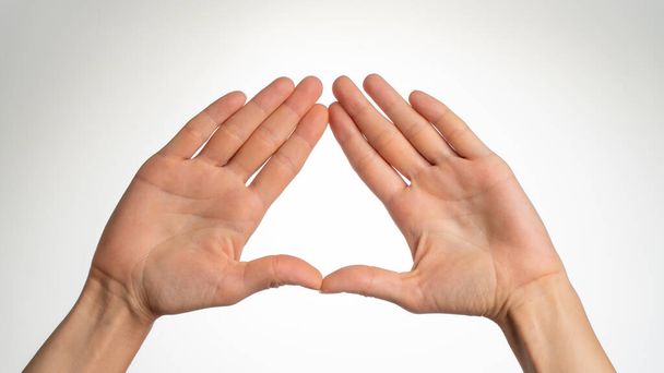 Handflächen einer Frau sind zu einem Dreieck auf weißem Hintergrund gefaltet. Hochwertiges Foto - Foto, Bild