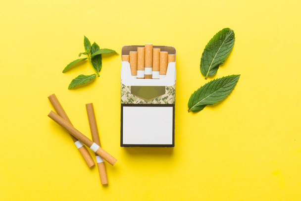 Pakket menthol sigaretten en verse munt op gekleurde tafel, Menthol sigaretten bovenaanzicht plat lay. - Foto, afbeelding