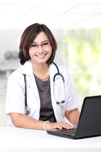 Woman doctor writing a clipboard while using laptop - Foto, Imagen