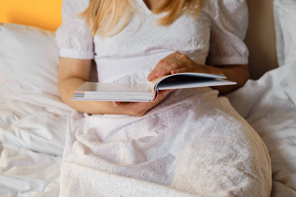 A girl reads a book in bed in the morning or before bedtime. Leisure and recreation concept. Close-up book in the hands of a girl. Place for your text - Fotografie, Obrázek