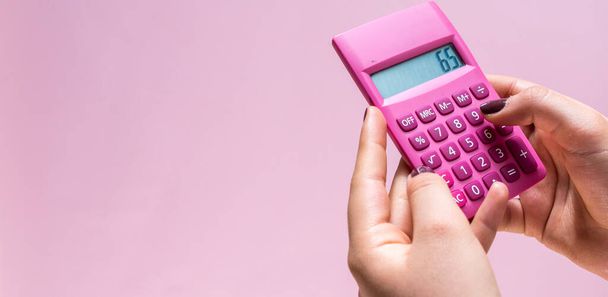 Hands using a pink calculator with white numbers on a pink surface - 写真・画像