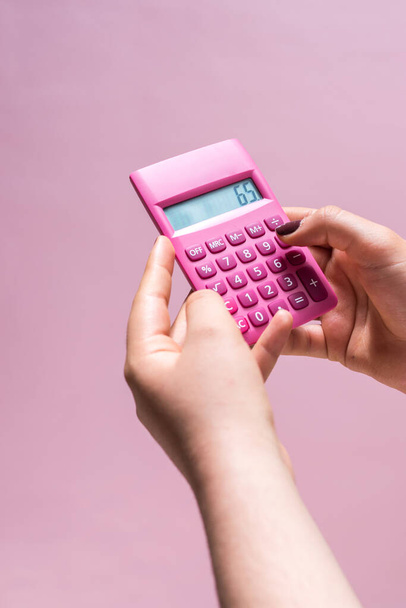 Hands using a pink calculator with white numbers on a pink surface - Valokuva, kuva