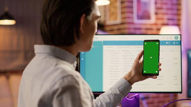 Άνδρας ελεύθερος επαγγελματίας κρατώντας smartphone με πράσινη οθόνη στην οθόνη. Κοιτάζοντας απομονωμένο φόντο copyspace με κενό chroma κλειδί και πρότυπο mockup στην οθόνη αφής του κινητού τηλεφώνου. - Φωτογραφία, εικόνα