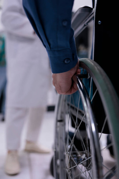 Selective focus on senior man living with disability in front of medical doctor for appointment in private hospital reception. Closeup of older man hand using wheelchair at medical clinic. - Foto, imagen
