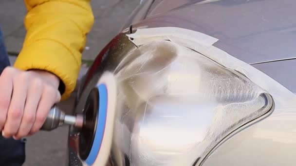 The hands of a young caucasian man in a yellow jacket are polishing with a detergent and a polishing machine the front headlight of a car, side view close-up in slow motion.Concept headlight polishing,polishing service. - Video, Çekim
