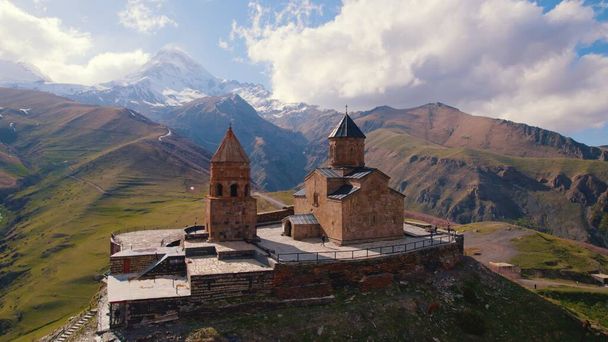 amazing aerial view of Gergeti Trinity Church surrounded by the Caucasus mountains in the sunny weather, Kazbegi, Georgia. High quality photo - Foto, immagini