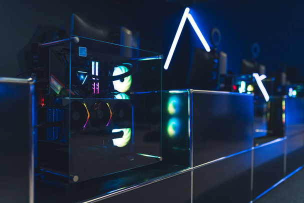 Professional gaming setup. Monitors and computers in trapnsparent case and colorful glowing fans. Blue neon lights. Horizontal shot. High quality photo - 写真・画像