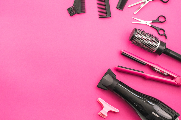 Scissors, combs, brushes, hair dryer, hair straightener and hairpin lie on the right in a semicircle on a pink background with copy space on the left, flat close-up. The concept of hairdressing. - Zdjęcie, obraz