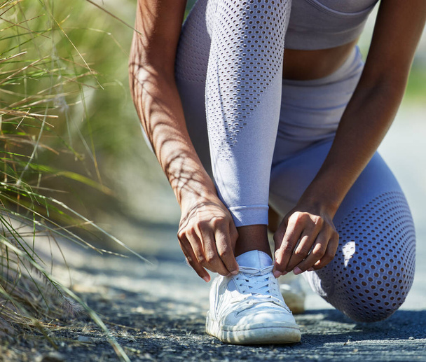 Readying herself for a serious run out in nature. Closeup shot of an unrecognisable woman tying her shoelaces while exercising outdoors - Photo, image