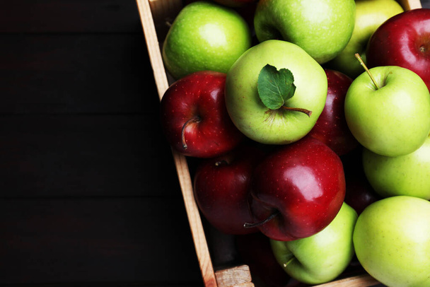 Fresh ripe red and green apples in wooden crate on black table, top view. Space for text - 写真・画像